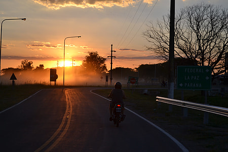 silhouette photo of person riding motorcycle on gray road thumbnail