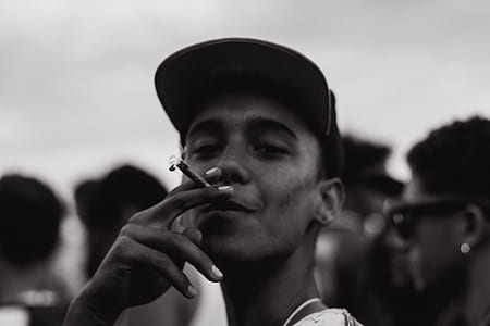 man wearing cap smoking cigar in grayscale photography thumbnail