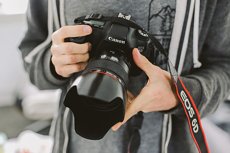 person in gray top holding black Canon EOS camera thumbnail