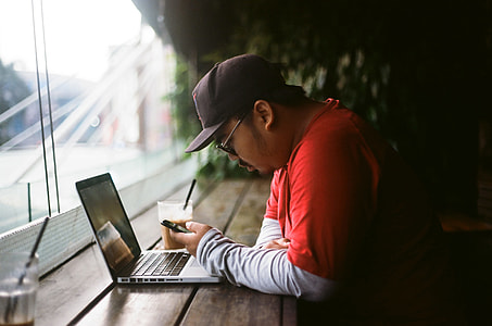 man sitting in front of laptop computer while operating smartphone thumbnail