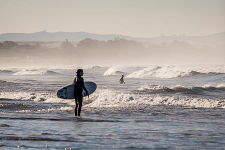 person with surfboard standing on body of water thumbnail