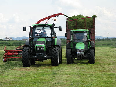 two green tractors towing attachments thumbnail