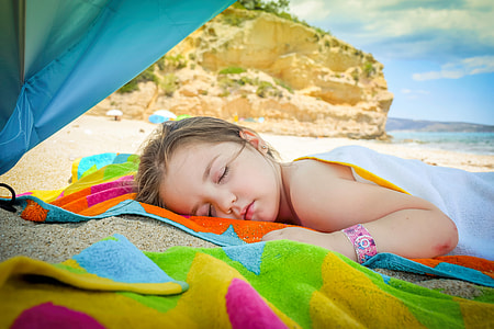 girl sleeping on orange, blue, and green textile near beach thumbnail