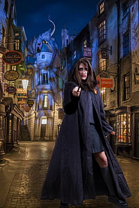photo of woman wearing black hoodie coat holding black wand standing beside concrete buildings thumbnail