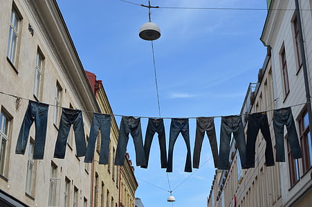 assorted-sizes denim jeans hanged on clothes line across two buildings at daytime thumbnail