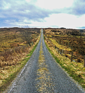 gray road between grassland during daytime thumbnail