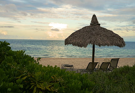 brown hut with two chairs near body of water thumbnail