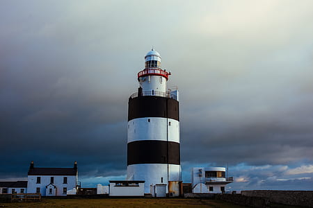 white and black lighthouse near white buildings under grey clouds thumbnail
