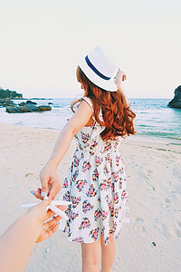 woman wearing white and red floral sleeveless mini dress and sun hat standing on seashore thumbnail