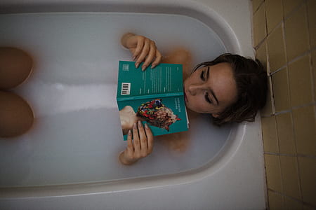 woman holding green covered book on white ceramic bathtub thumbnail