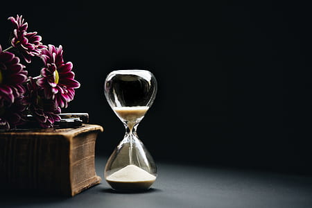 clear hourglass beside brown book and red flowers thumbnail