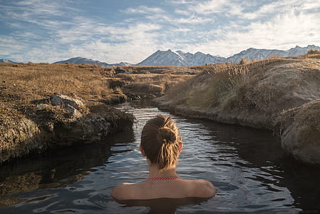 topless woman in body of water between brown grass field under cloudy sky thumbnail
