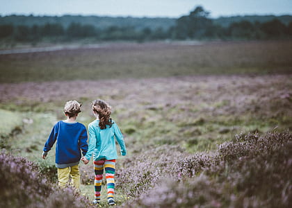 boy and girl holding hands while walking on grass open field during daytime thumbnail