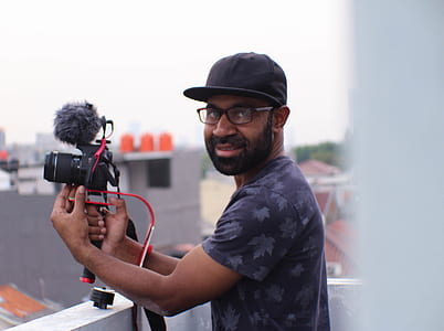 man holding black DSLR camera standing beside white wall thumbnail