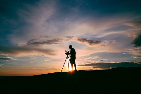 silhouette photo of person setting up camera on tripod thumbnail