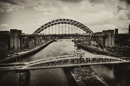 grayscale photography of ship crossing under bridge during cloudy daytime thumbnail