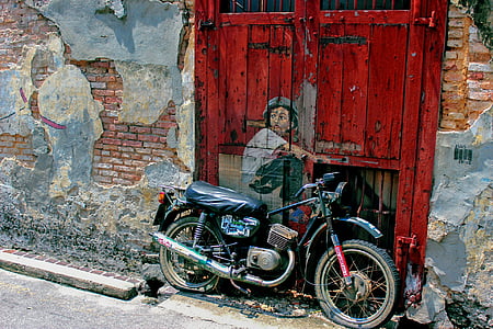 boy in white shirt painted in red wooden door beside motorcycle thumbnail