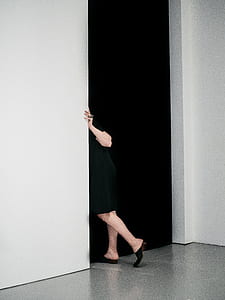 woman in black dress peaking beside white wall thumbnail