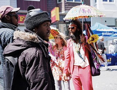 man on black bobble hat and black parka jacket standing next to man wearing maroon hat thumbnail