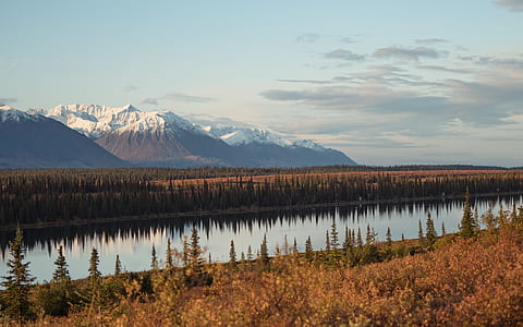 brown field near river and snow-covered mountains thumbnail