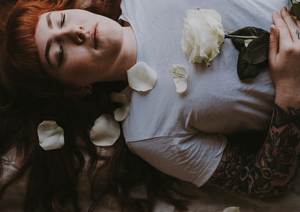 woman wearing grey shirt lying on the field holding white rose thumbnail