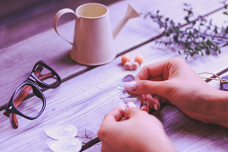 person holding package near eyeglasses and watering can on wooden surface thumbnail