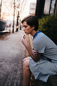 woman sitting beside road holding cigarette stick thumbnail