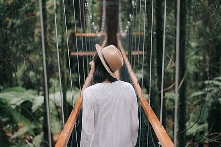 back of woman wearing brown hat and grey sweatshirt crossing bridge thumbnail