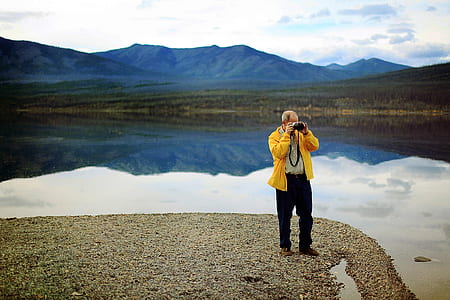 man standing near lake while holding camera thumbnail