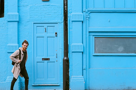 man with backpack walking beside blue building thumbnail