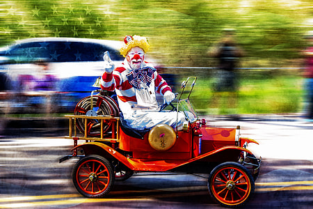 clown riding car waving hand while driving on road during daytime thumbnail