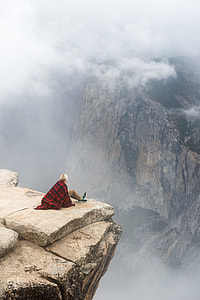 person sitting on edge of cliff during daytime thumbnail