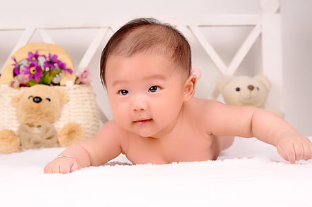 baby on bed near white and brown bear plush tiys thumbnail