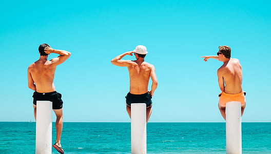 three men each sitting on poles by the sea thumbnail