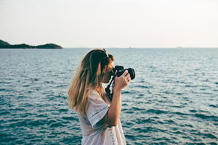 woman standing while taking photo using black DSLR camera near body of water at daytime thumbnail