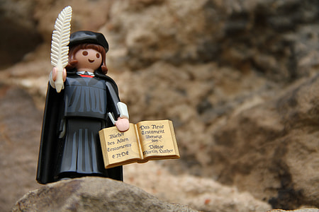 black and multicolored plastic woman wearing academic gown holding book and feather pen figurine on beige rock selective focus photo thumbnail