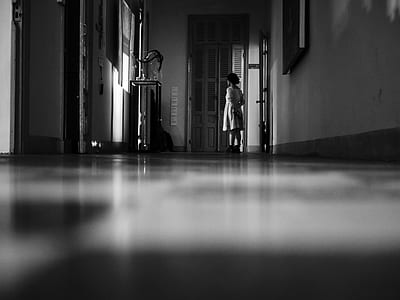 grayscale photography of girl standing near door inside room thumbnail