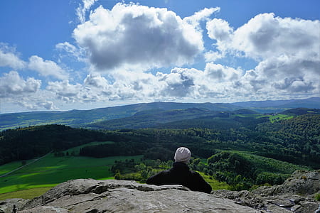 person sitting on mountain in front of green leafed trees during daytime thumbnail