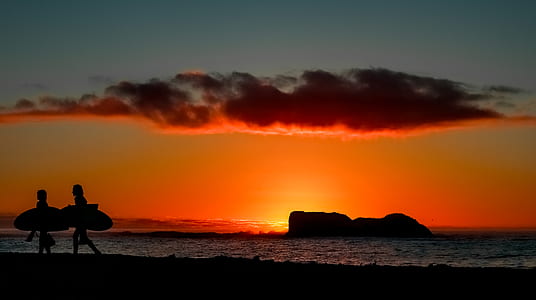 silhouette of two person walking on seashore while holding surfboards thumbnail