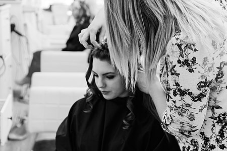 grayscale photo of woman arranging hair of woman sitting while looking down thumbnail