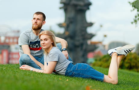 man sitting beside woman lying on grass during daytime thumbnail