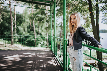 Blonde woman in a black jacket and ripped jeans by a green handrail thumbnail