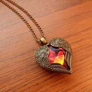 gold-colored necklace and heart pendant on wooden table thumbnail