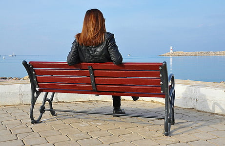 woman sitting on black and red wooden bench looking on wide open body of water thumbnail