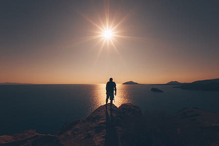 silhouette of man standing on cliff in front of ocean during golden hour thumbnail