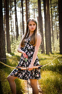 woman wearing tank mini dress holding composite bow and arrow in forest thumbnail