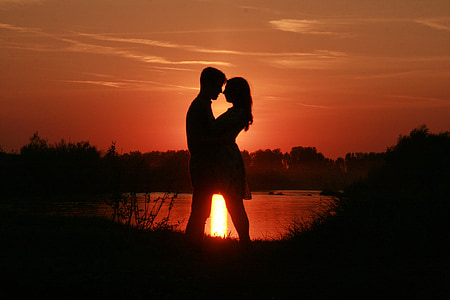 silhouette of couple standing beside body of water against sun ray thumbnail