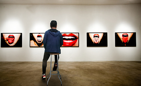 person wearing blue hoodie sitting in brown wooden stool in front of lips photo gallery thumbnail