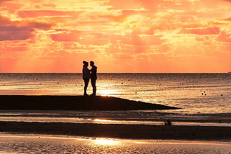 silhouette of man and woman on shore under orange sunset thumbnail