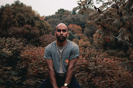 man wearing gray crew-neck t-shirt sits behind green leaf plants thumbnail